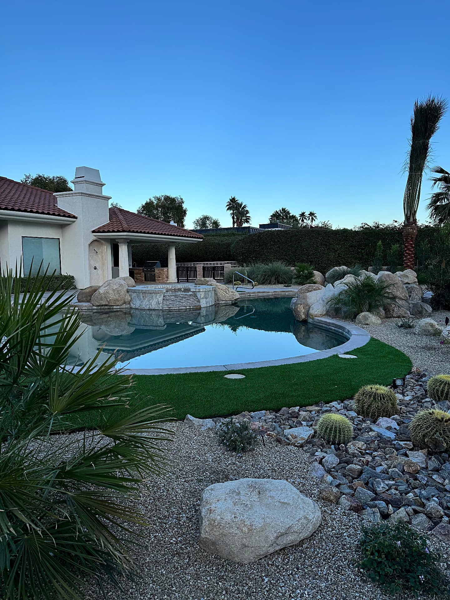 Dusk backyard pool framed by boulders, gravel beds and a curved artificial turf lawn
