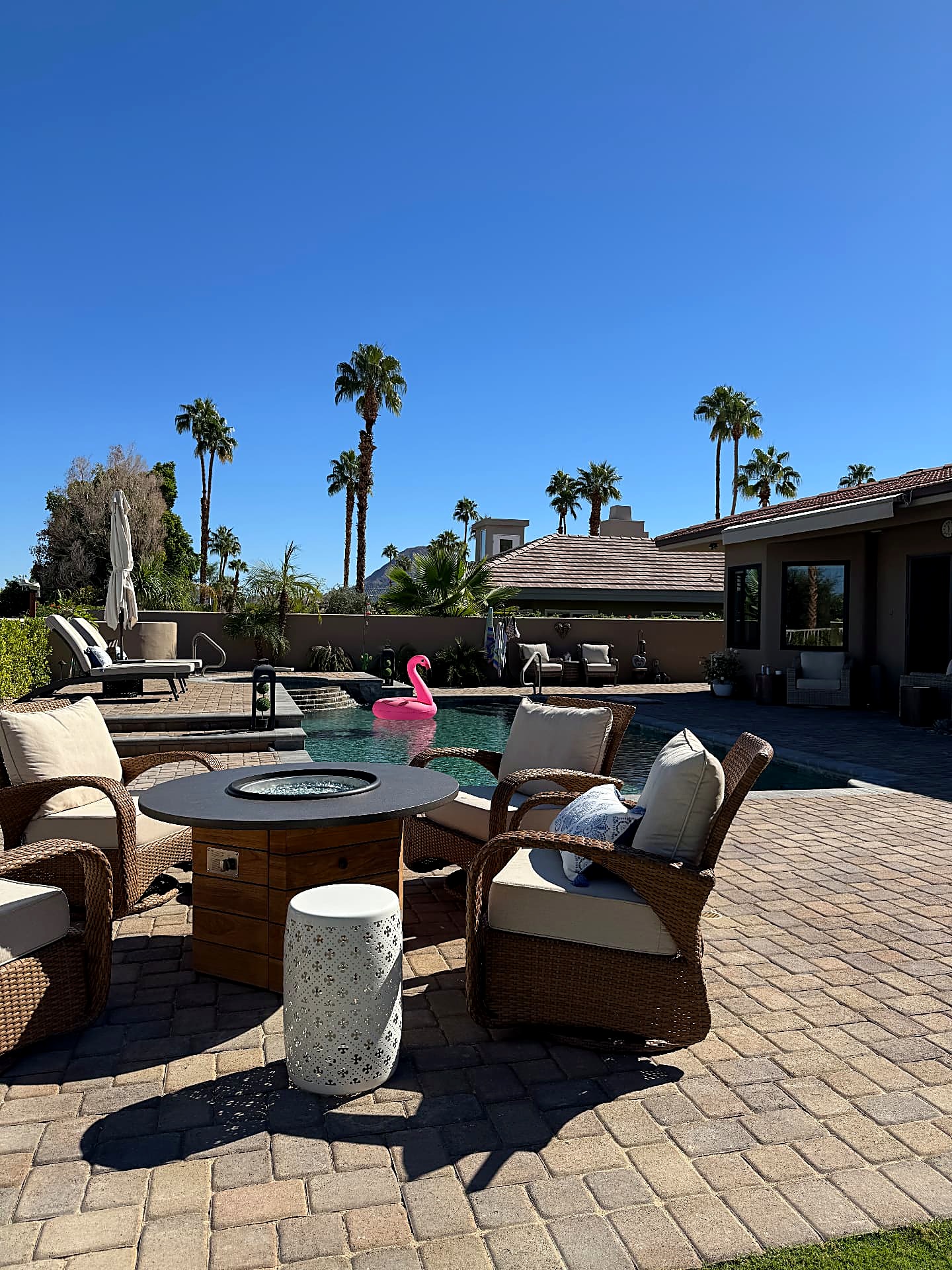 After — backyard patio of stone pavers with fire table seating beside the pool