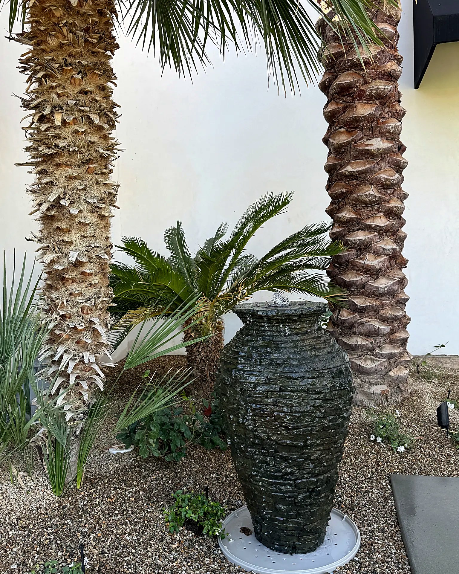 Stacked stone fountain urn set in a gravel bed between palm trunks