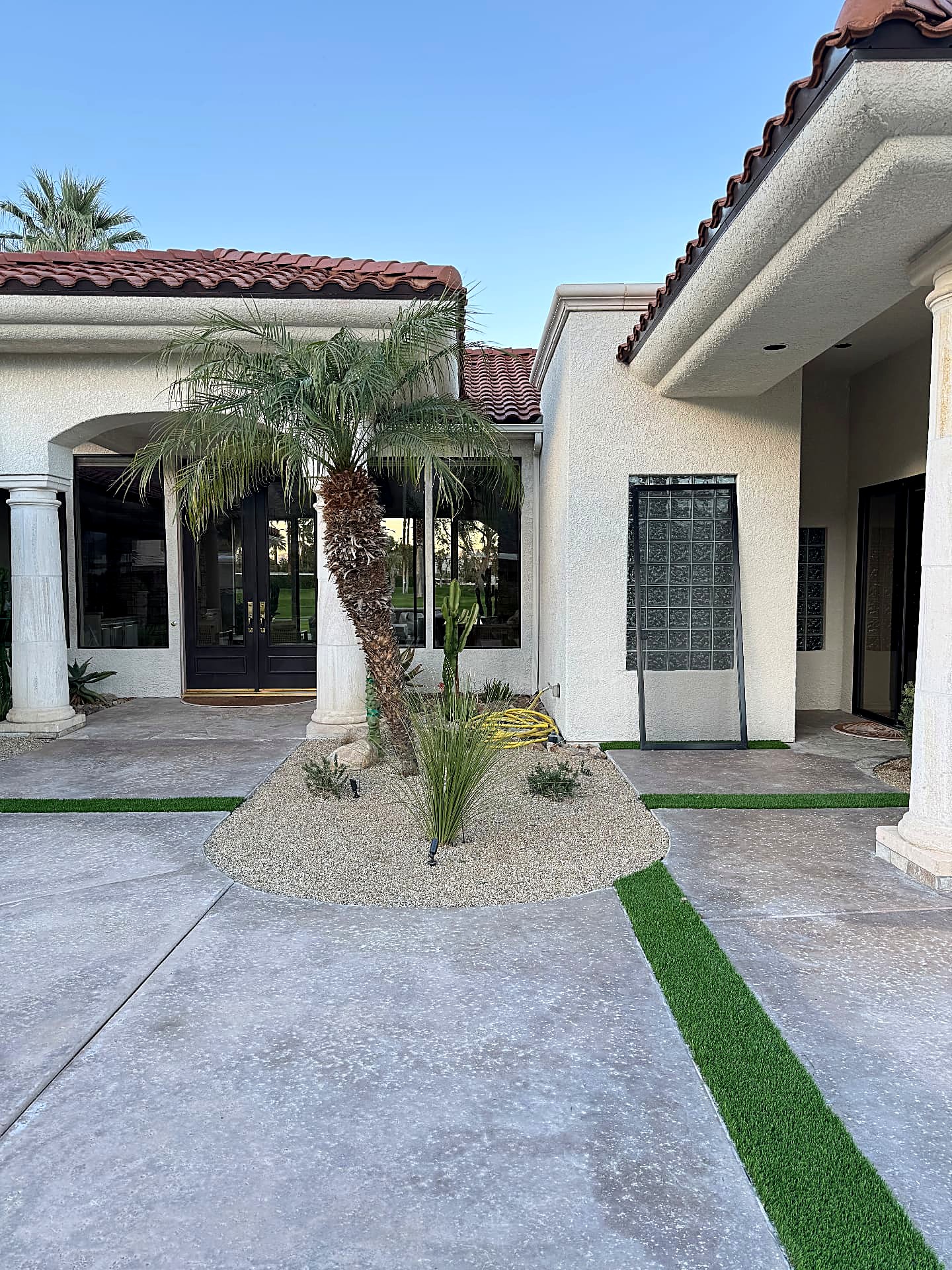 Front entry with curved gravel bed, palm and desert plantings between concrete drives