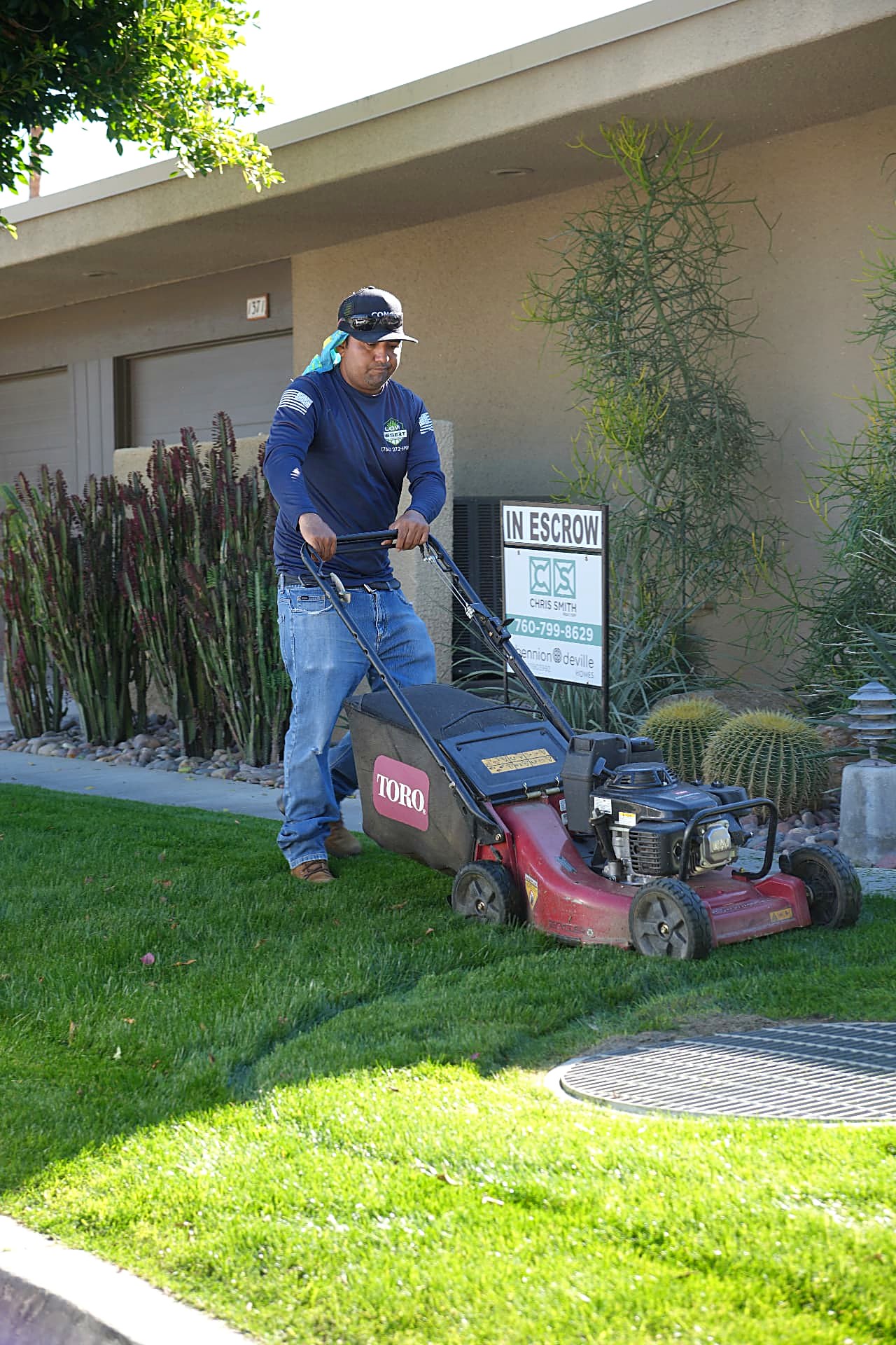 Crew member pushing a mower across a front lawn beside desert plantings